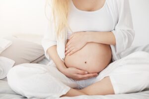 Schüßler Salze: Schüßler Salze für Frauen Schüßler Salze: young pregnant soon be mother touching her belly sitting her bedroom afternoon pregnancy concept